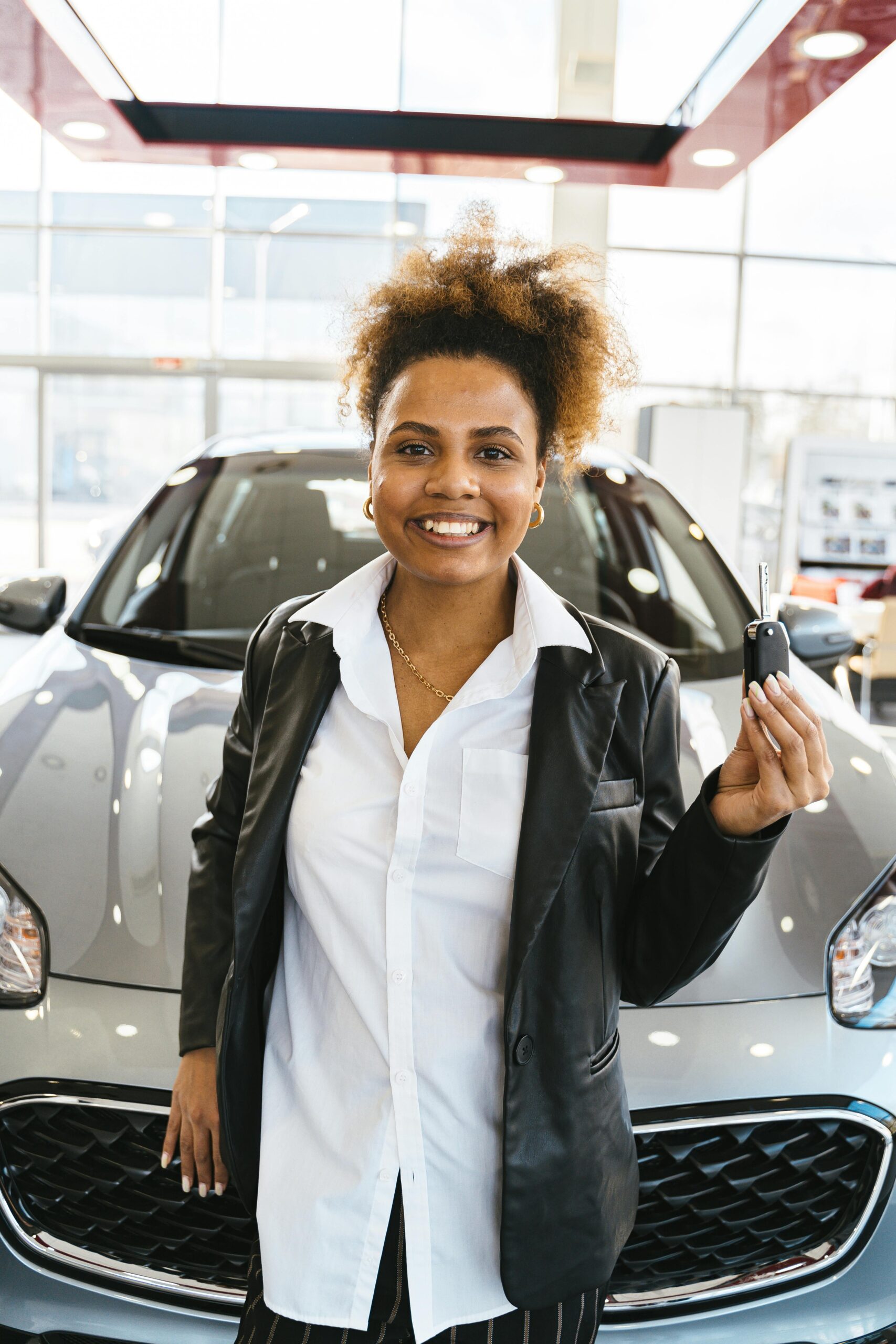 Smiling woman in a car dealership holding keys to her new vehicle.